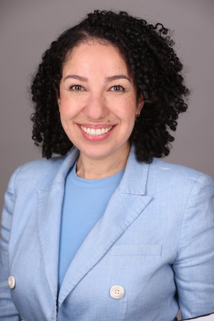 Diana Rodriguez has dark curly hair and wears a light blue suit