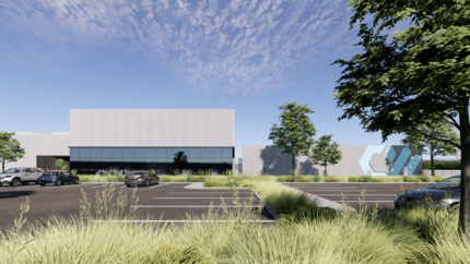 A large data center building with tall grass, trees, and a parking lot in the foreground and blue skies overhead.