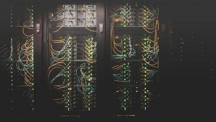 Close-up image of data center servers in black mesh cabinets many wires and lights visible inside.